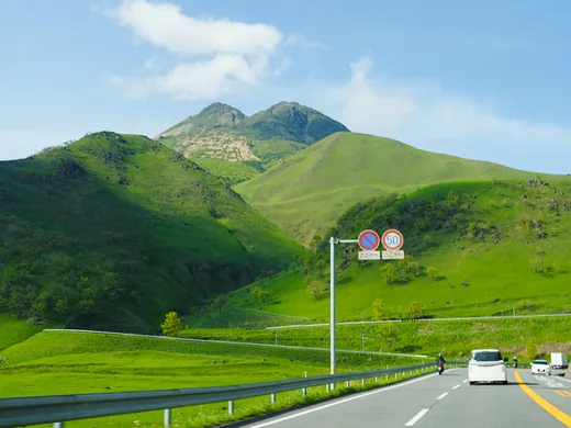 Straße vor grünen Hügeln und dem Doppelgipfel des Yufu-dake in Kyushu