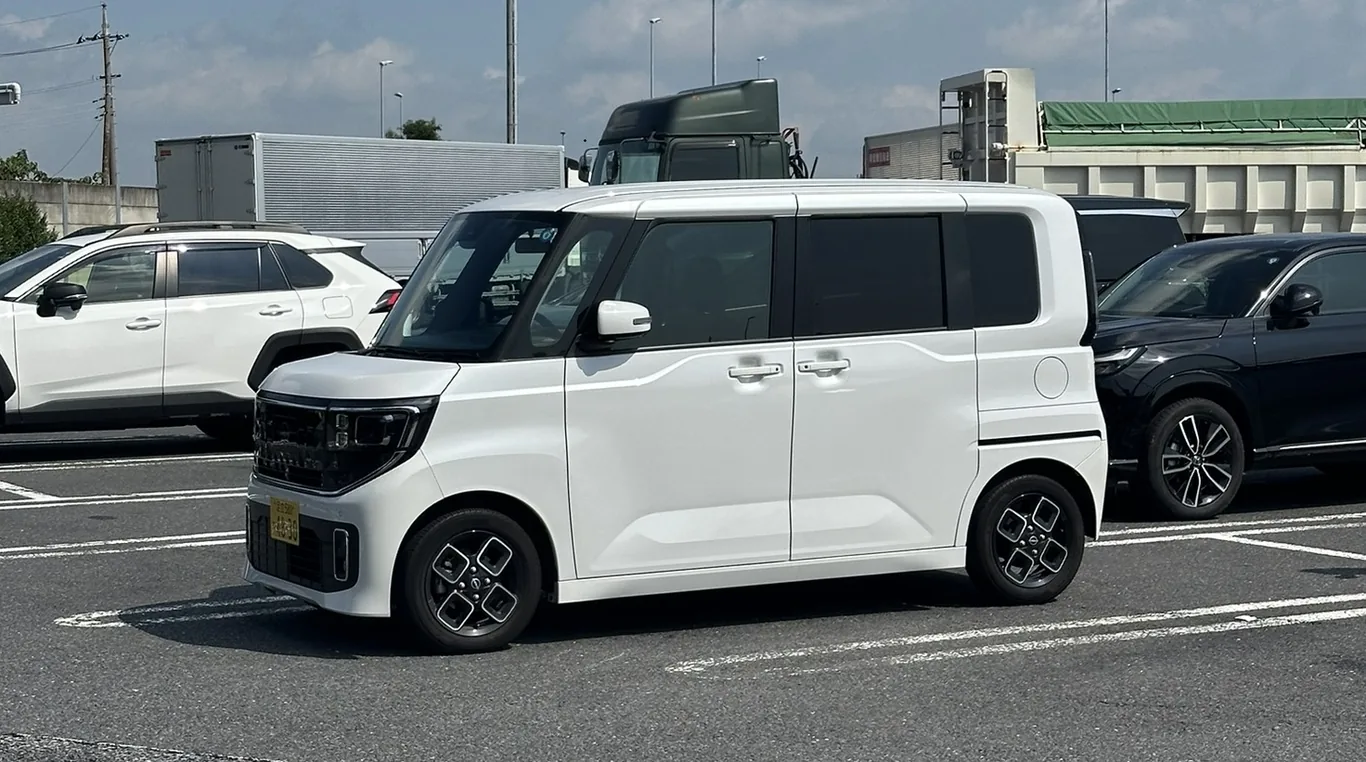 Weißes, kastenförmiges Kleinstauto mit gelbem Kennzeichen auf einem Parkplatz