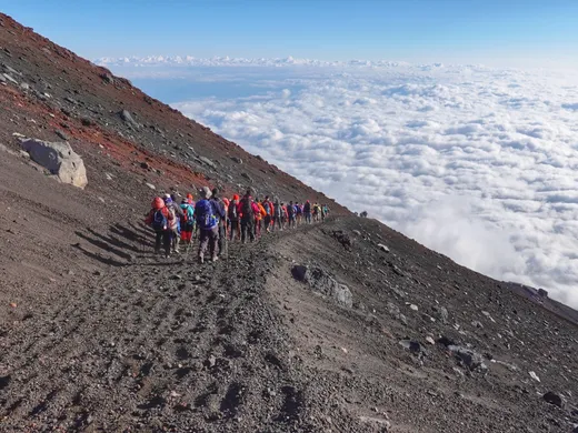 Bergsteiger auf dem Weg zum Gipfel des Fuji, daneben ein Meer aus Wolken