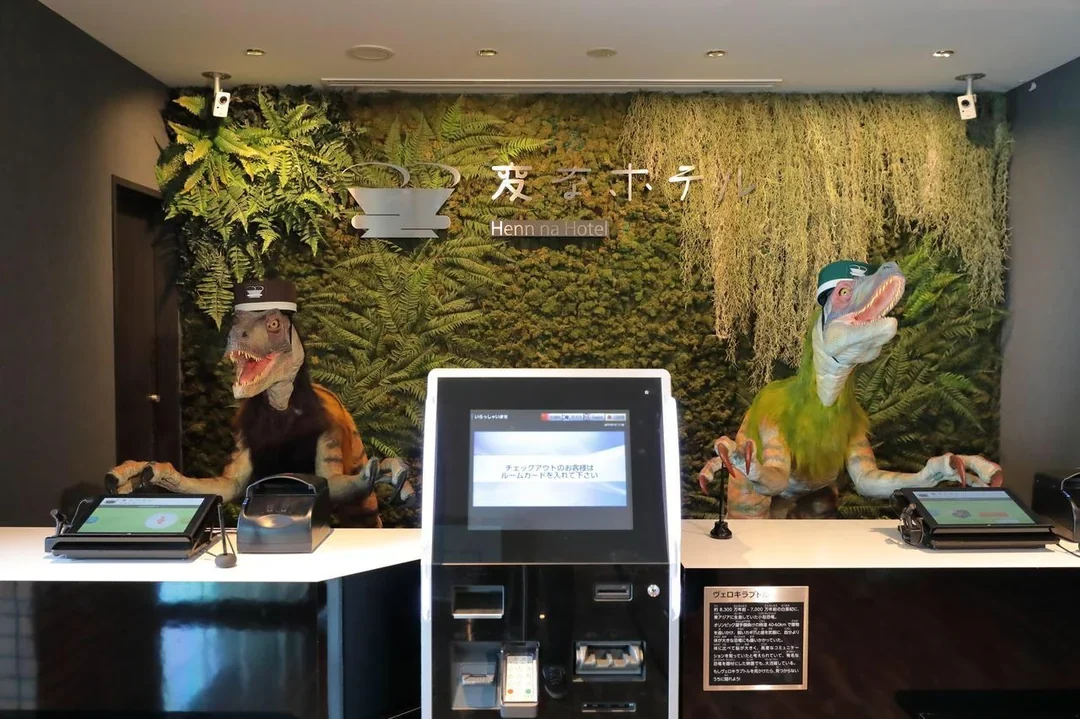 Rezeption des Henn na Hotel mit zwei Dinosaurier-Robotern hinter dem Tresen, dazwischen ein Automat zum Einchecken, im Hintergrund eine Pflanzenwand
