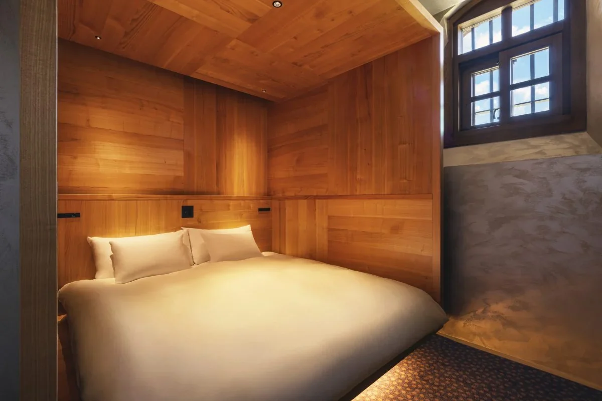 Schlafbereich einer Suite mit holzverkleideten Wänden, Doppelbett und einem kleinen hochsitzenden Fenster