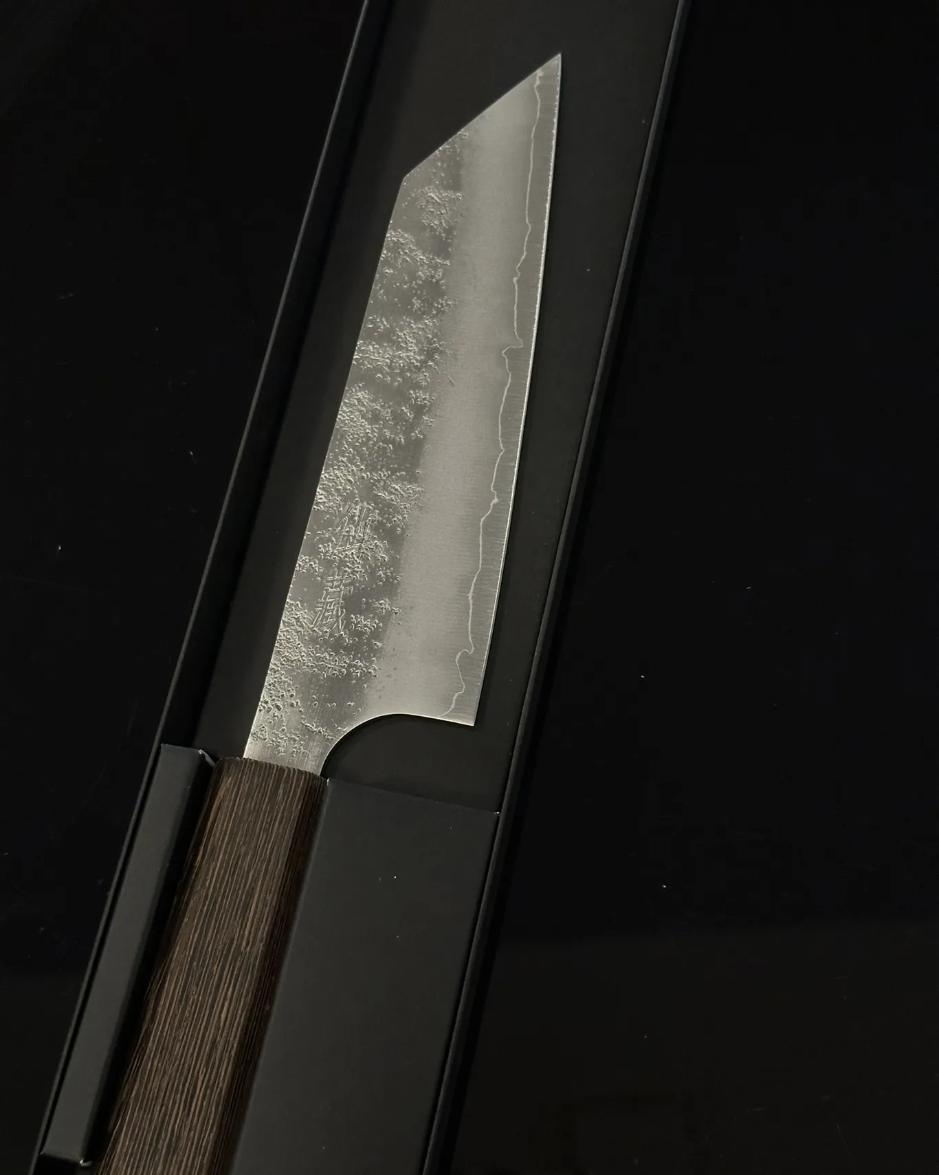 Japanisches Küchenmesser mit gehämmerter Klinge, abgeschrägter Spitze und dunklem Holzgriff in einer schwarzen Geschenkschachtel