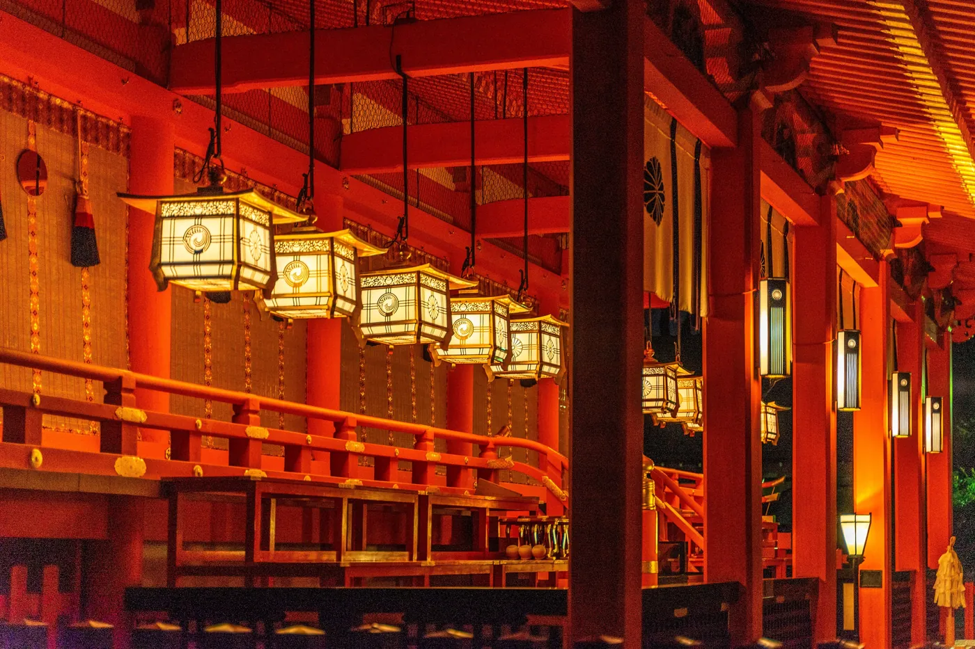 Beleuchtete Papierlaternen unter dem Vordach einer zinnoberroten Schreinhalle bei Nacht