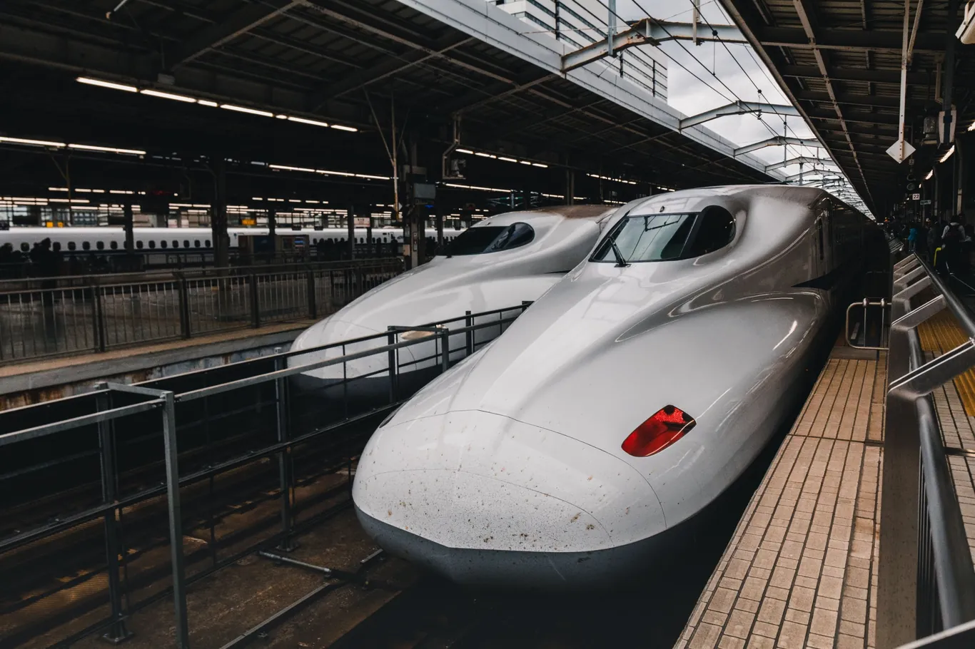 Zwei weiße Shinkansen-Züge nebeneinander am Bahnsteig unter einem Stahldach