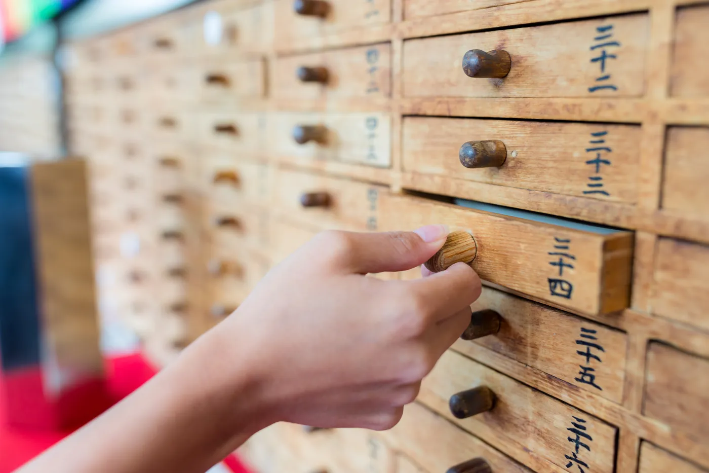 Eine Hand öffnet eine von vielen kleinen Holzschubladen, die mit japanischen Zahlen beschriftet sind