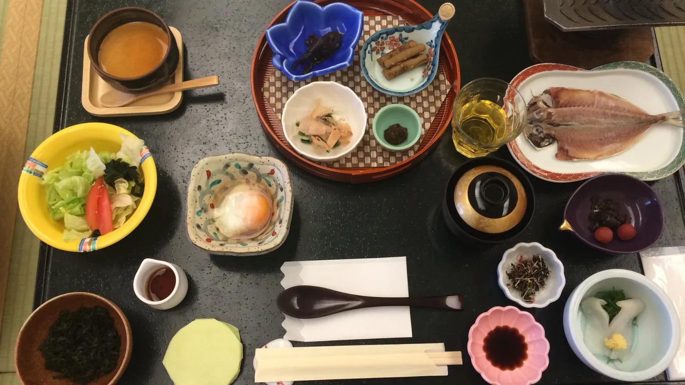 Japanisches Frühstück von oben: gegrillter Fisch, Miso-Suppe, Salat, Ei und viele kleine Schälchen auf einem Tablett