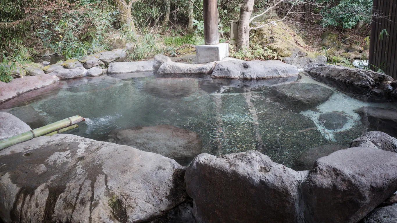 Ein Außenbad aus Naturstein mit klarem Wasser, umgeben von Felsen und Grün