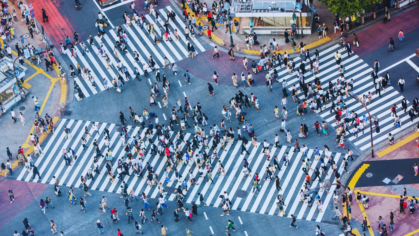 Blick von hoch oben auf die Kreuzung von Shibuya, Menschen auf den weißen Zebrastreifen in alle Richtungen