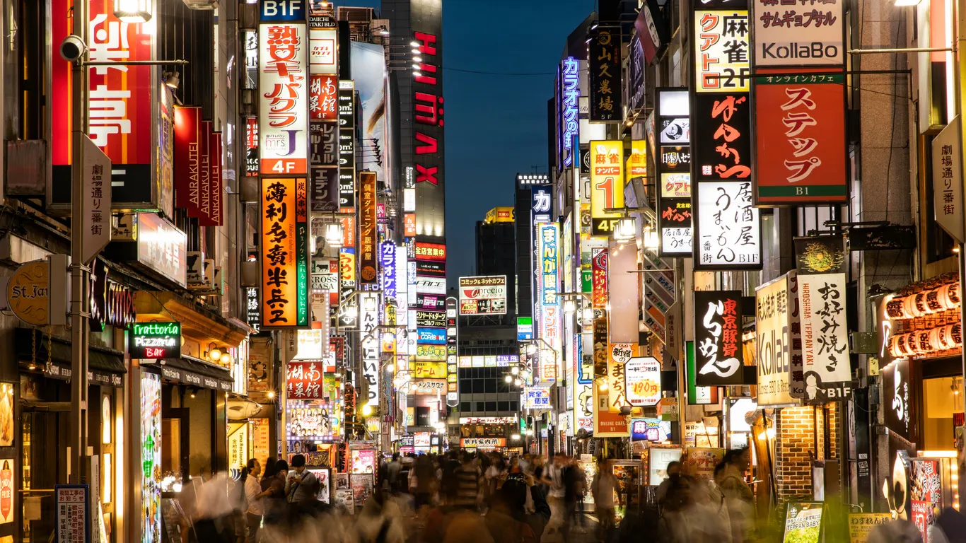 Eine Straße in Shinjuku bei Nacht mit unzähligen leuchtenden Schildern und vielen Menschen